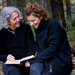 Two women smiling in woods with book